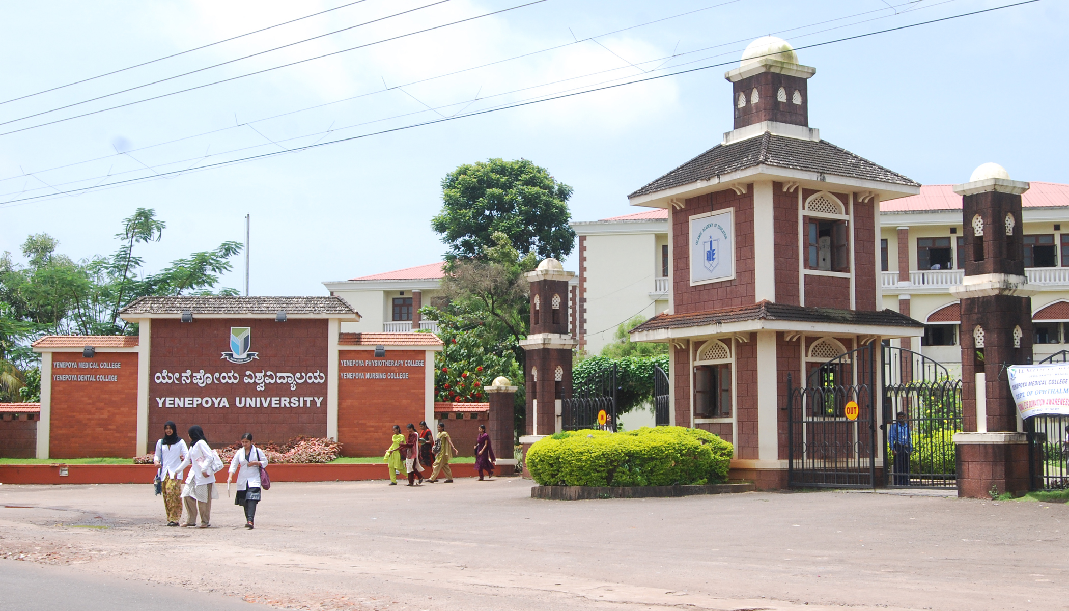 Yenepoya University entrance with the university sign, brick gatehouse and students